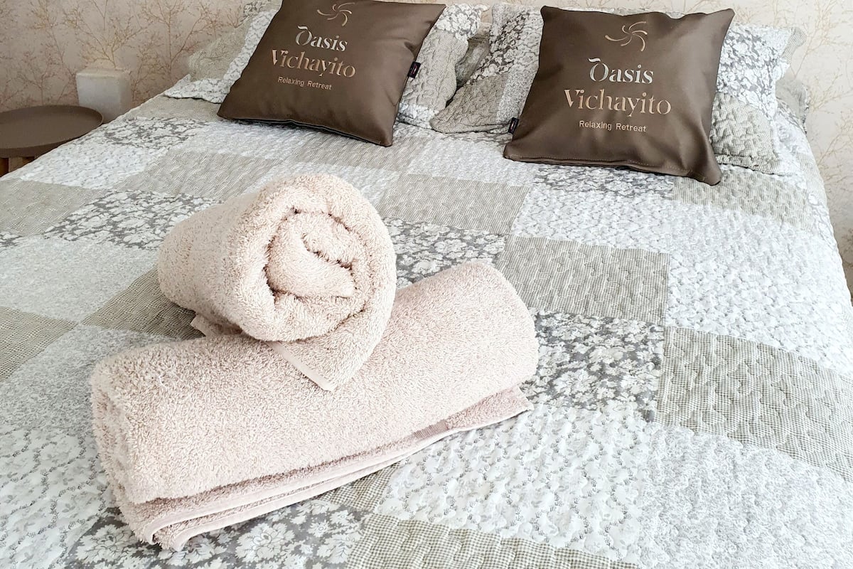 A neatly made bed with a patterned bedspread, two brown pillows with text, and a rolled towel on the bed.