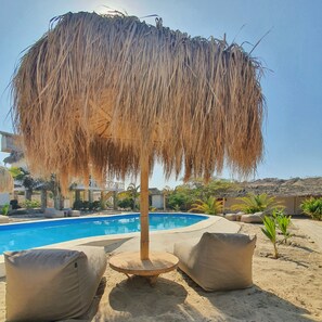 A pool area with a thatched umbrella, lounge chairs, and a clear blue pool. - Oasis de Vichayito (Los Organos)