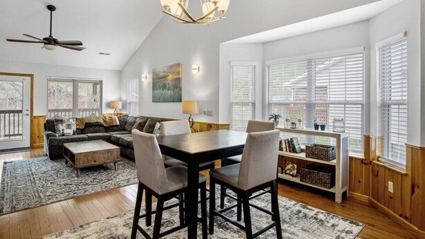 A spacious living room with a dark wooden dining table, comfortable seating, a ceiling fan, and large windows with blinds. - River Bear-Riverfront in Pigeon Forge (Pigeon Forge)