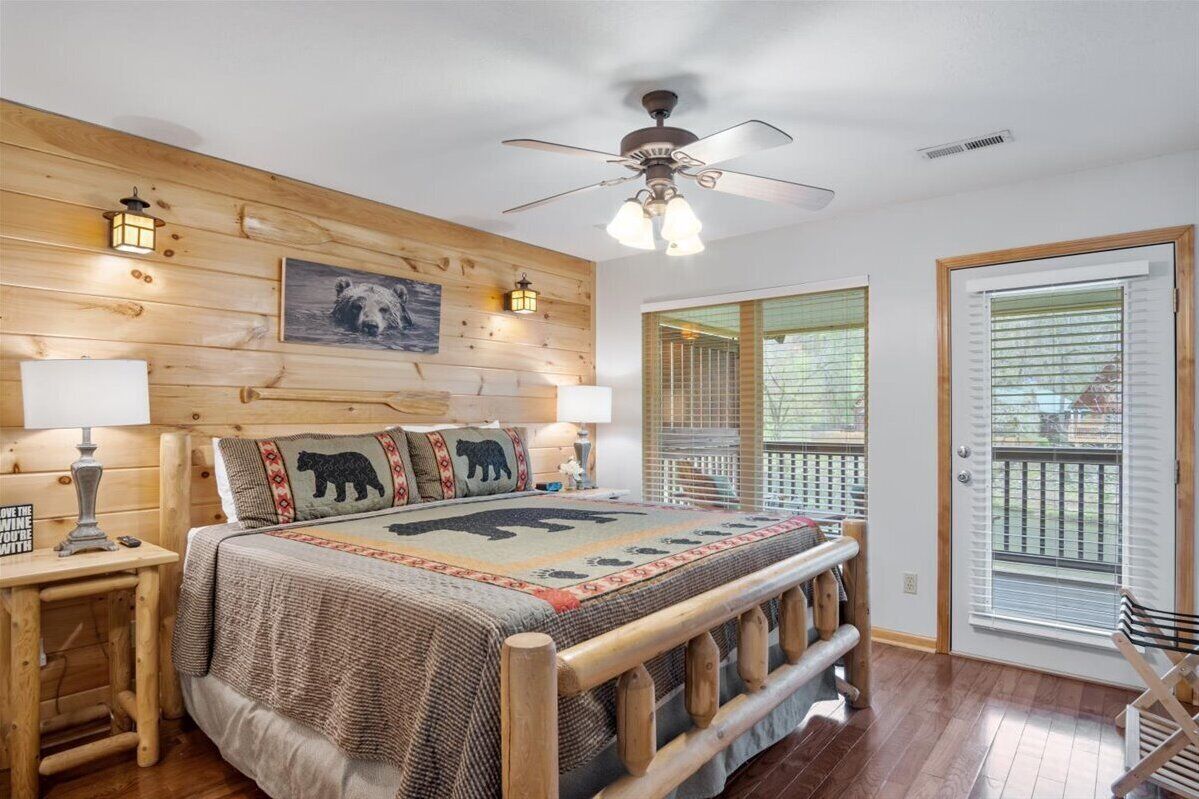 A bedroom with a wooden headboard, a bed with a bear-themed blanket, a ceiling fan, and a view of the outdoors through a sliding glass door.