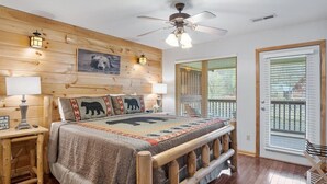 A bedroom with a wooden headboard, a bed with a bear-themed blanket, a ceiling fan, and a view of the outdoors through a sliding glass door. - River Bear-Riverfront in Pigeon Forge (Pigeon Forge)