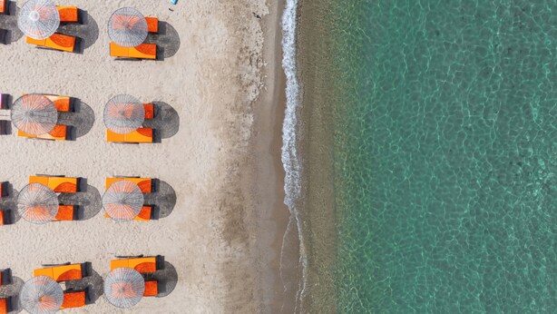 An aerial view of a beach with rows of orange and grey beach umbrellas aligned along the shoreline. - Asterina Hotel (Bodrum)