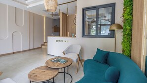 A modern reception area with a reception desk labeled "RECEPTION," a white chair, a teal sofa, and a round wooden table. - Asterina Hotel (Bodrum)