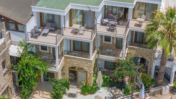 Un hotel de varios pisos con balcones, mobiliario exterior y abundante vegetación.