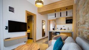 A modern living room with a flat-screen TV, a round wooden coffee table, and a sofa with teal cushions. - Asterina Hotel (Bodrum)