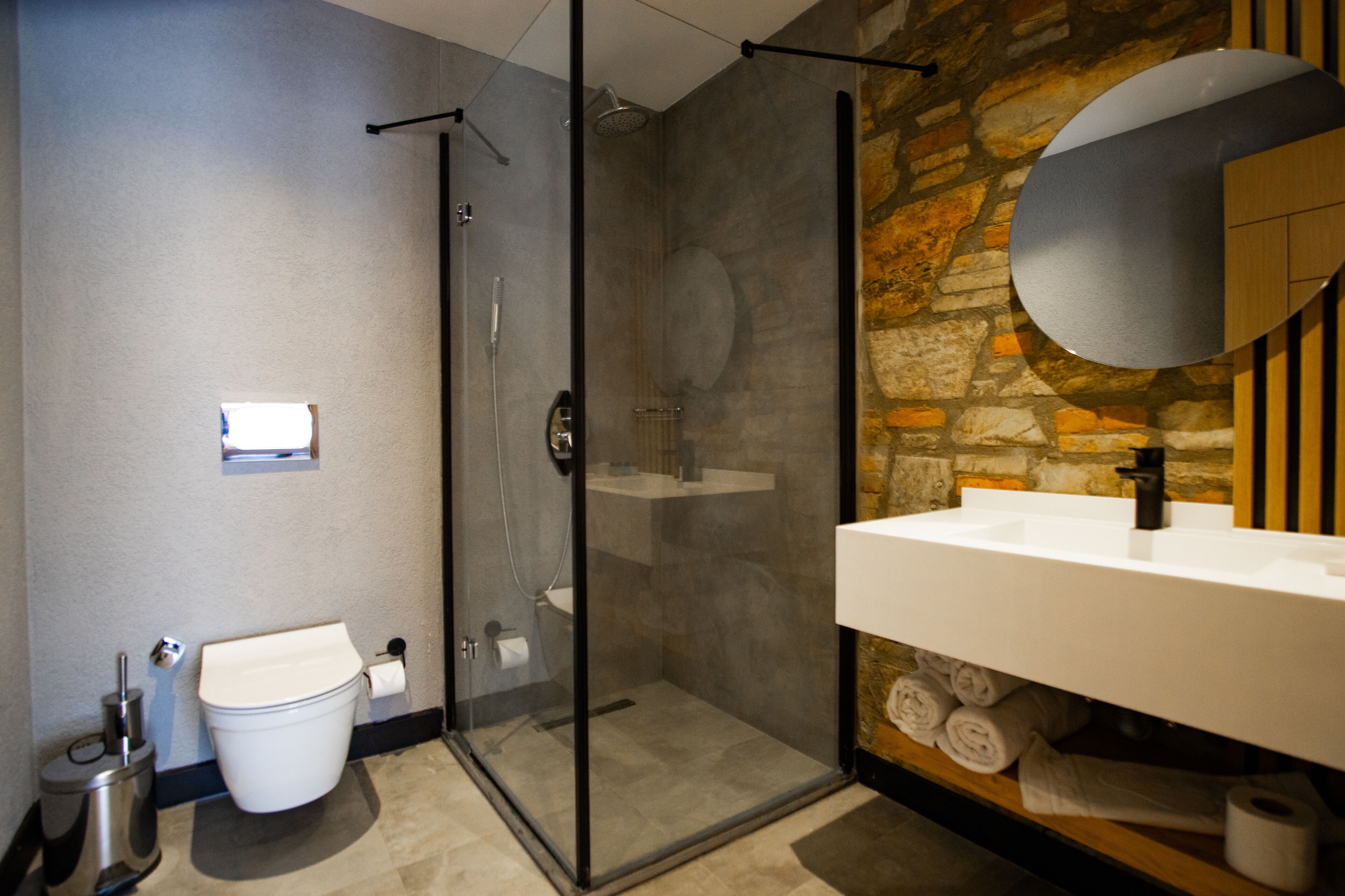 Un baño moderno con ducha de vidrio, lavamanos blanco y pared de piedra de fondo.