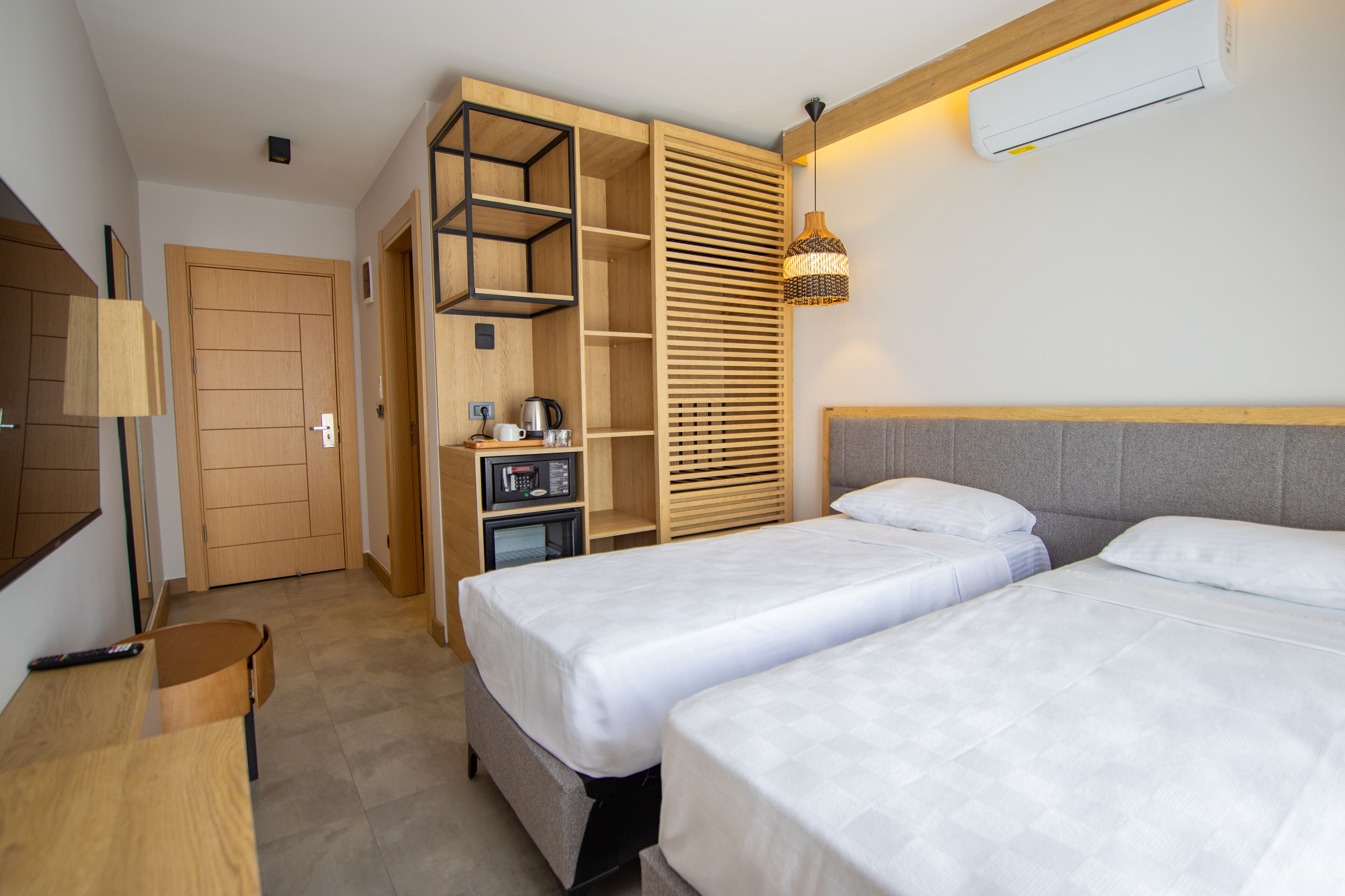 Une chambre d’hôtel avec deux lits, une armoire en bois, un bureau, une lampe et un appareil de climatisation.