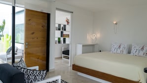 A modern bedroom with a large bed, a bedside table with a lamp, a built-in bookshelf, and a sliding glass door leading to a balcony. - Siaan Betine 4br Deluxe PDC  (Playa del Carmen)