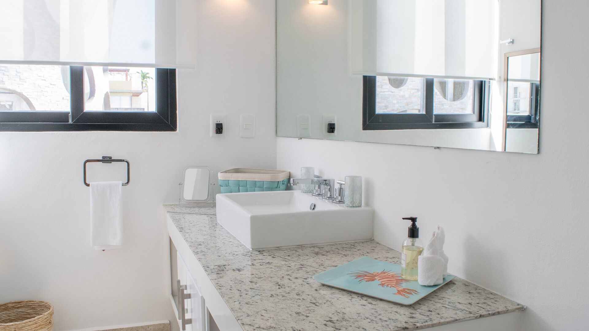 Un baño moderno con un espejo grande, un lavamanos blanco y una encimera con una toalla y artículos de aseo.