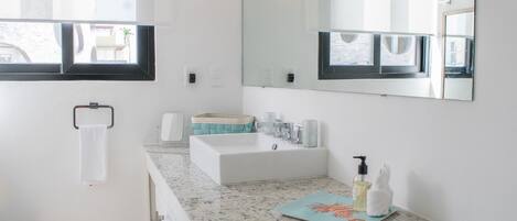 Un baño moderno con un espejo grande, un lavamanos blanco y una encimera con una toalla y artículos de aseo.