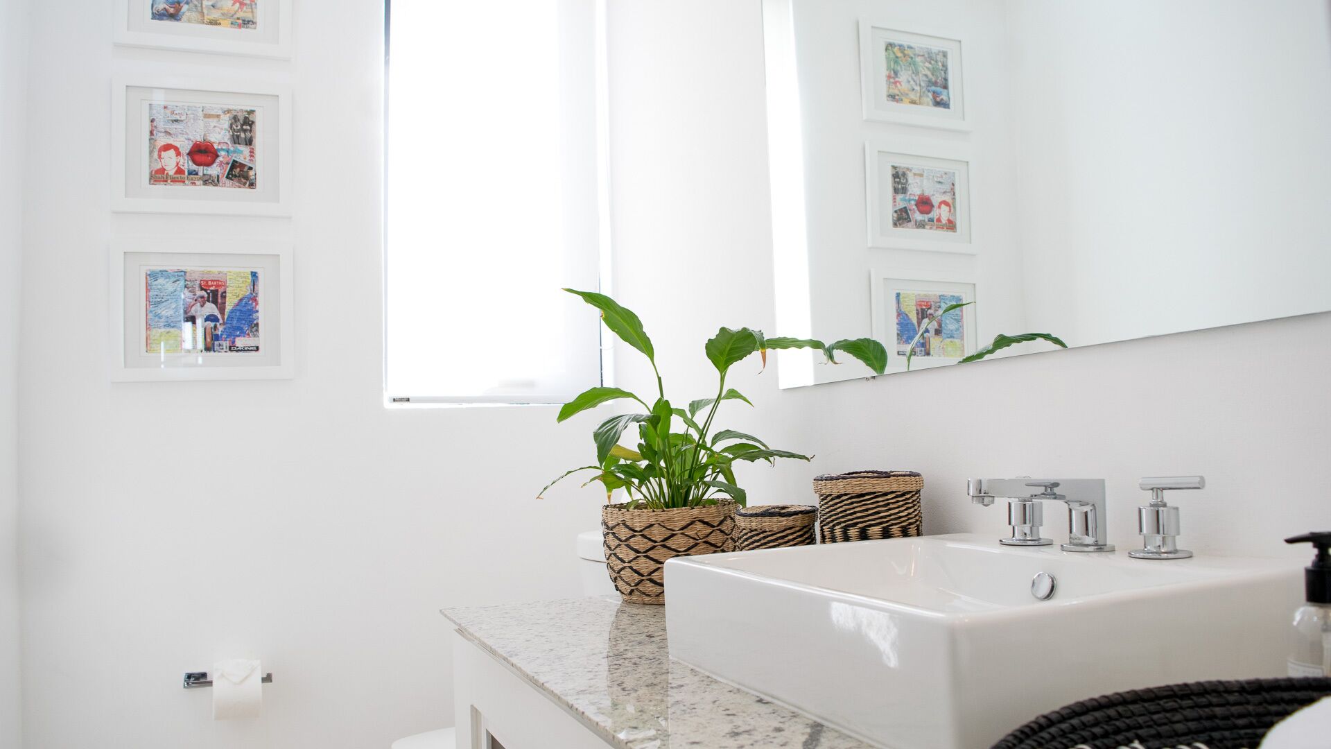 A modern bathroom with a white sink, a large mirror, and framed artwork on the wall.
