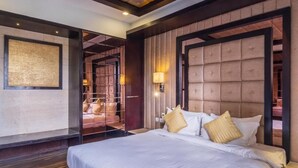Une chambre d’hôtel avec un grand lit, un plancher en bois, un téléviseur fixé au mur et une porte donnant accès à la salle de bain.