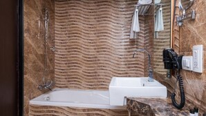 Une salle de bain moderne avec un mur ondulé en marbre, une baignoire, un lavabo et un miroir.