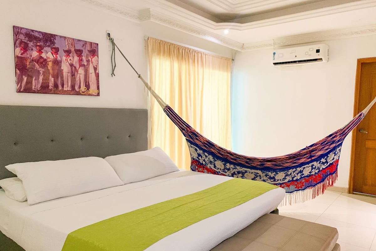 Un dormitorio con cama, hamaca, un cuadro y aire acondicionado.