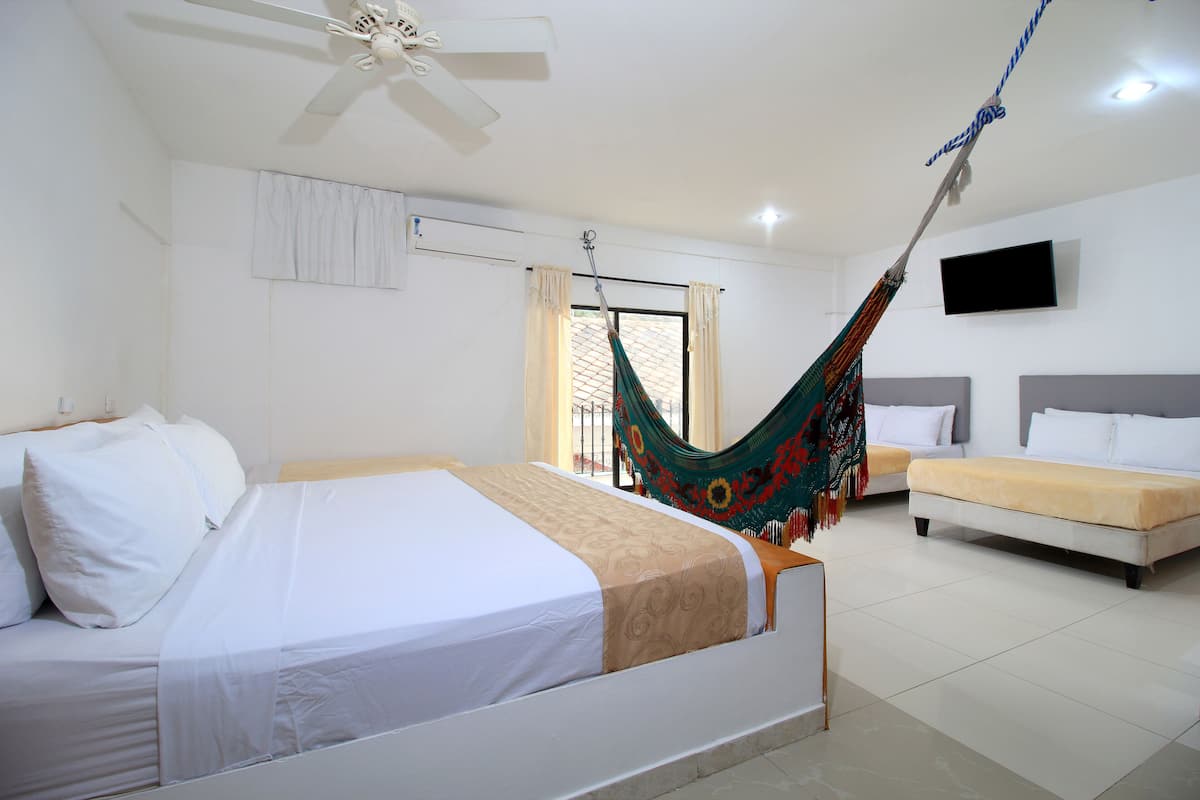 Habitación de hotel con cama, sofá, hamaca, ventilador de techo, televisor y ventana con cortinas.