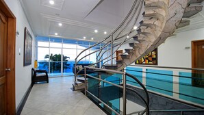 Ein modernes Interieur mit einer Wendeltreppe, einem Glasgeländer und Blick durch große Fenster.