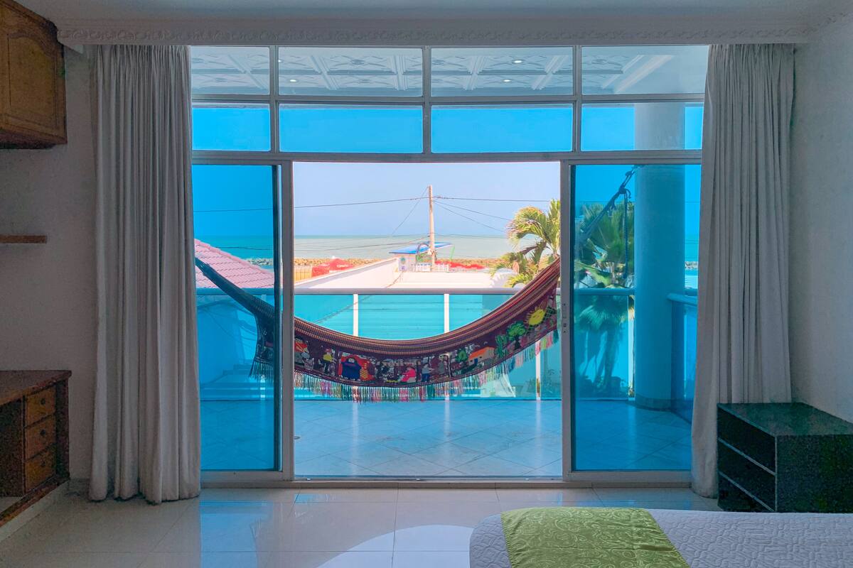 Una habitación con un amplio ventanal corredero que da a un balcón con una hamaca.