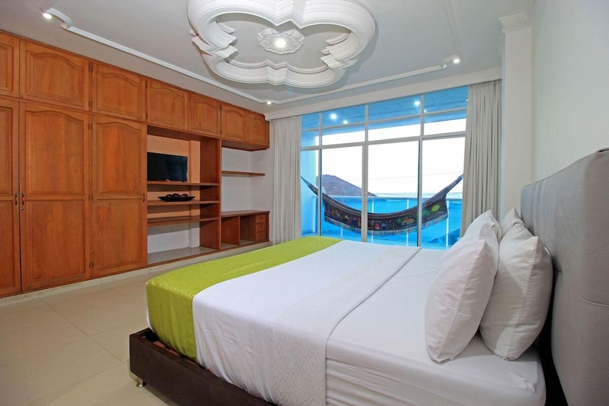 Ein Hotelzimmer mit einem großen Bett, einem Holzschrank und Meerblick durch ein großes Fenster.