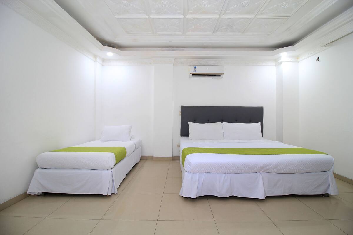 Una habitación de hotel con dos camas individuales, una cama grande, paredes blancas, un techo con diseño decorativo y un equipo de aire acondicionado instalado en el techo.