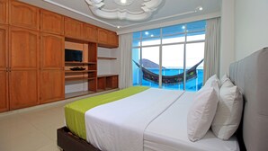 Ein Hotelzimmer mit einem großen Bett, einem Holzschrank und Blick auf das Meer durch ein großes Fenster.
