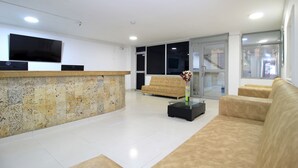 A modern living room with a stone accent wall, a flat-screen TV, a sofa, and a coffee table with a vase. - Hotel Rodadero Inn By GEH Suites (Santa Marta)