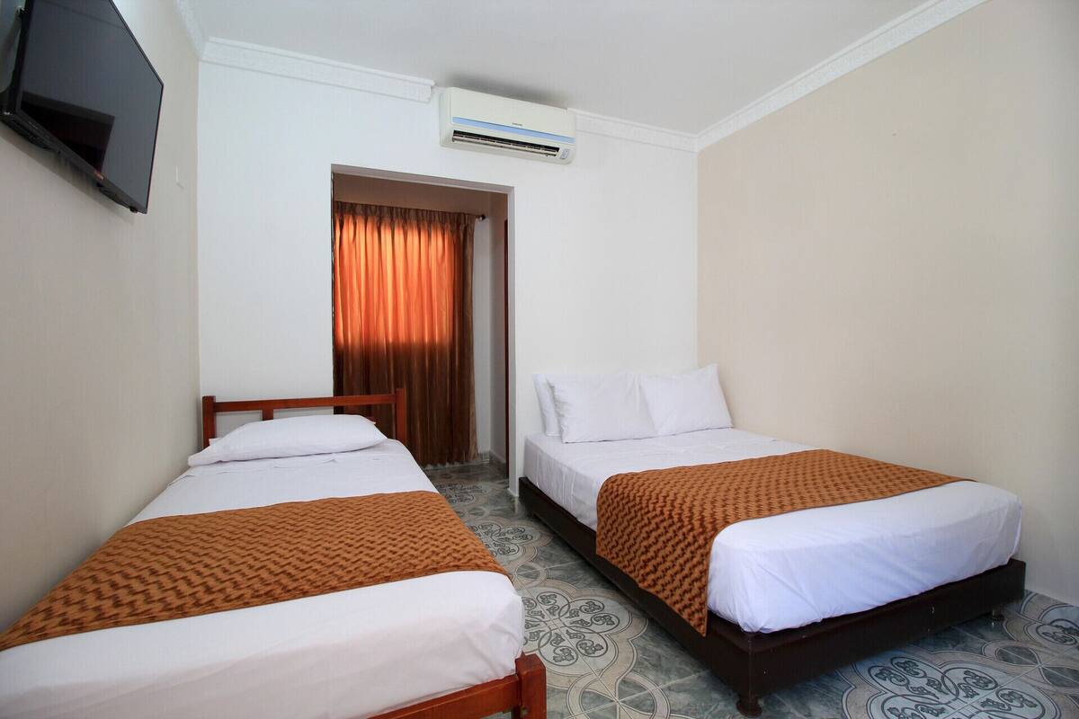 A hotel room with two beds, a TV, an air conditioning unit, and a patterned floor.