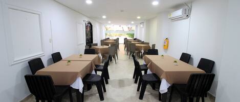 Un salón de conferencias con varias mesas y sillas, paredes blancas y piso de baldosas.
