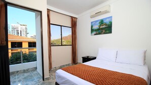 A hotel room with a large bed, a painting on the wall, a window with curtains, and an air conditioning unit. - Hotel Rodadero Inn By GEH Suites (Santa Marta)