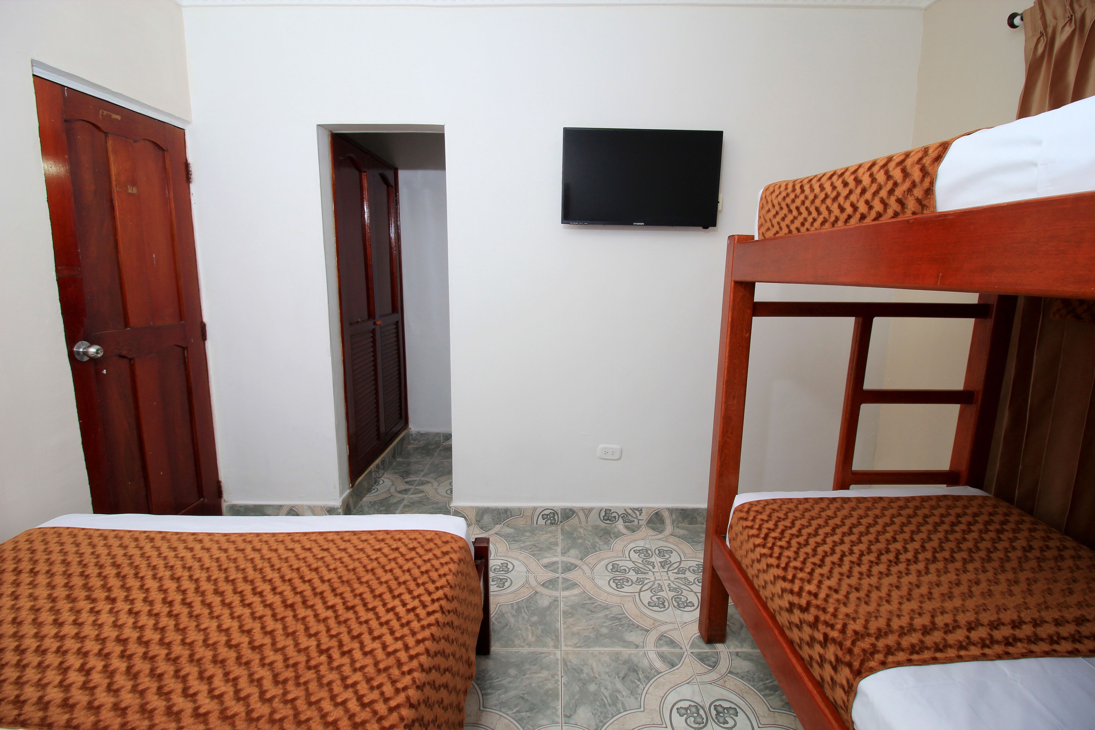 Una habitació amb dos llits superposats, una televisió penjada a la paret i una porta que dona a una altra habitació.