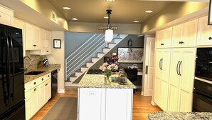 A modern kitchen with granite countertops, white cabinetry, a central island, and a staircase leading to another level. - BY THE BAY (Annapolis)