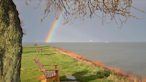 A wooden chair by a grassy lakeside with a rainbow in the background. - BY THE BAY (Annapolis)