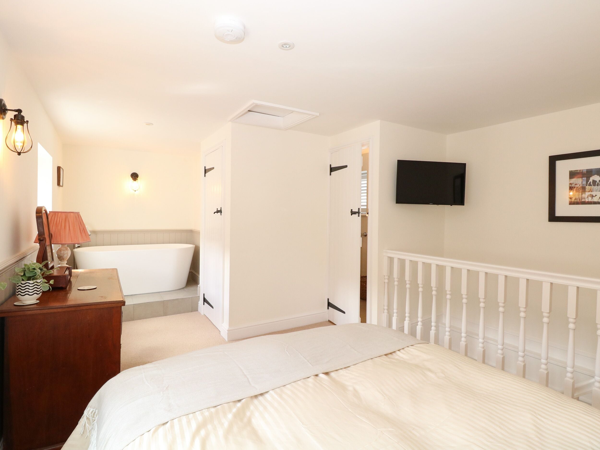 Un dormitorio con cama, mesita de noche, lámpara, televisor, puerta y baño con bañera.