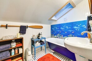 A bathroom with a bathtub, a sink, a shelf with toiletries, a towel rack, and a blue wall mural. - Cozy Catskills Vacation Rental with Deck! (Fleischmanns)