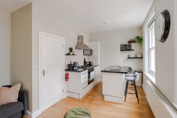 A compact kitchen with a microwave, stove, and island with stools.