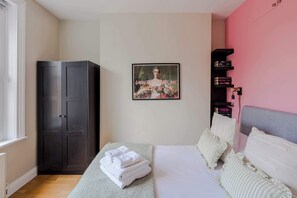 A bedroom with a bed, a wardrobe, a framed picture on the wall, and a bookshelf.