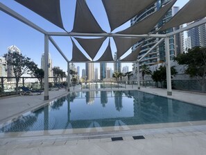 An indoor swimming pool with a modern design, surrounded by a covered area with a view of tall buildings.