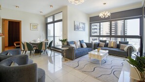 Una sala de estar moderna con sofá, sillas, una mesa de comedor y grandes ventanales que ofrecen vistas de la ciudad.