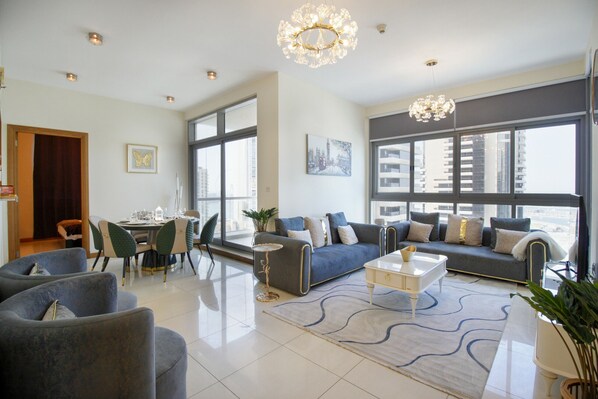 A modern living room with a sofa, chairs, a dining table, and large windows offering a city view.