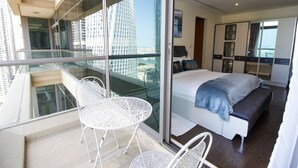 Una habitación de hotel moderna con balcón, una cama con manta azul y vistas a edificios altos.