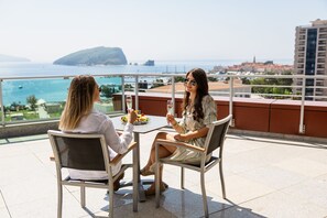 Two people seated at a table with a view of the sea and buildings in the background. - Hotel Tq Plaza (Budva)