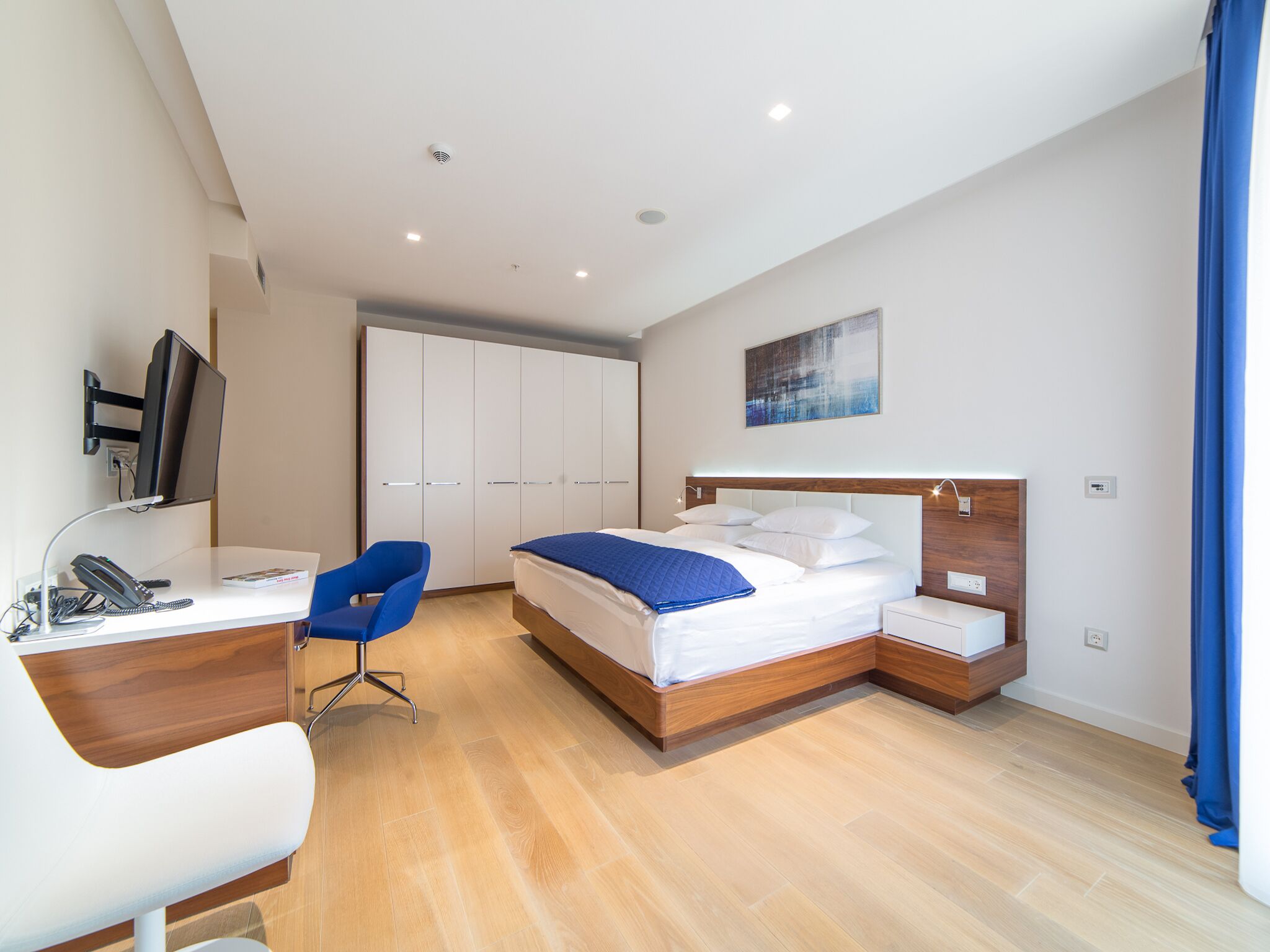Ein modernes Hotelzimmer mit Schreibtisch, Stuhl, Bett, Kleiderschrank und einem Bild an der Wand.
