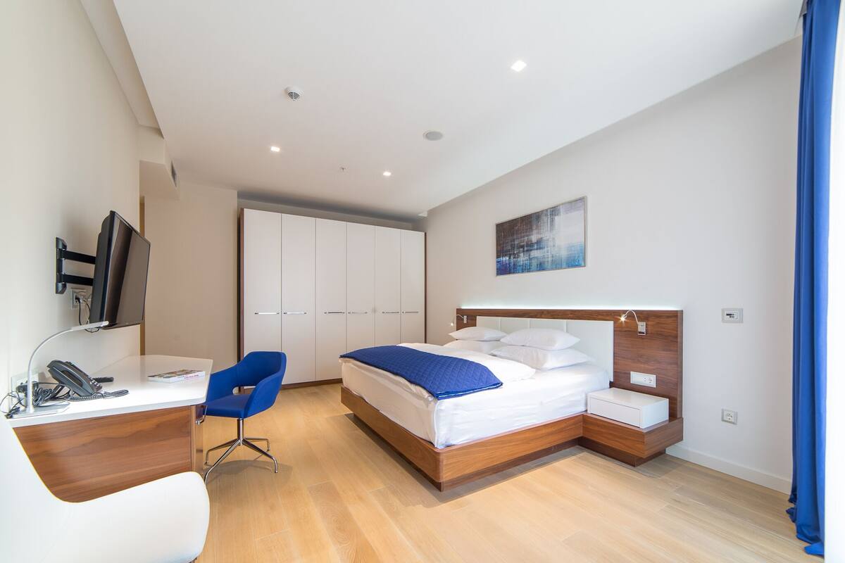 Une chambre d’hôtel moderne équipée d’un bureau, d’une chaise, d’un lit, d’une armoire et ornée d’un tableau au mur.
