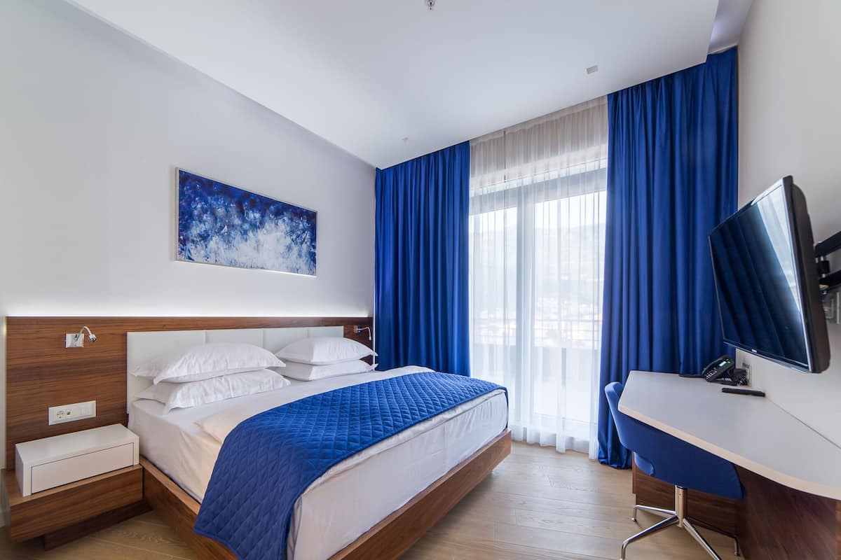 Une chambre d’hôtel avec un lit, un bureau, une télévision et une fenêtre avec des rideaux.