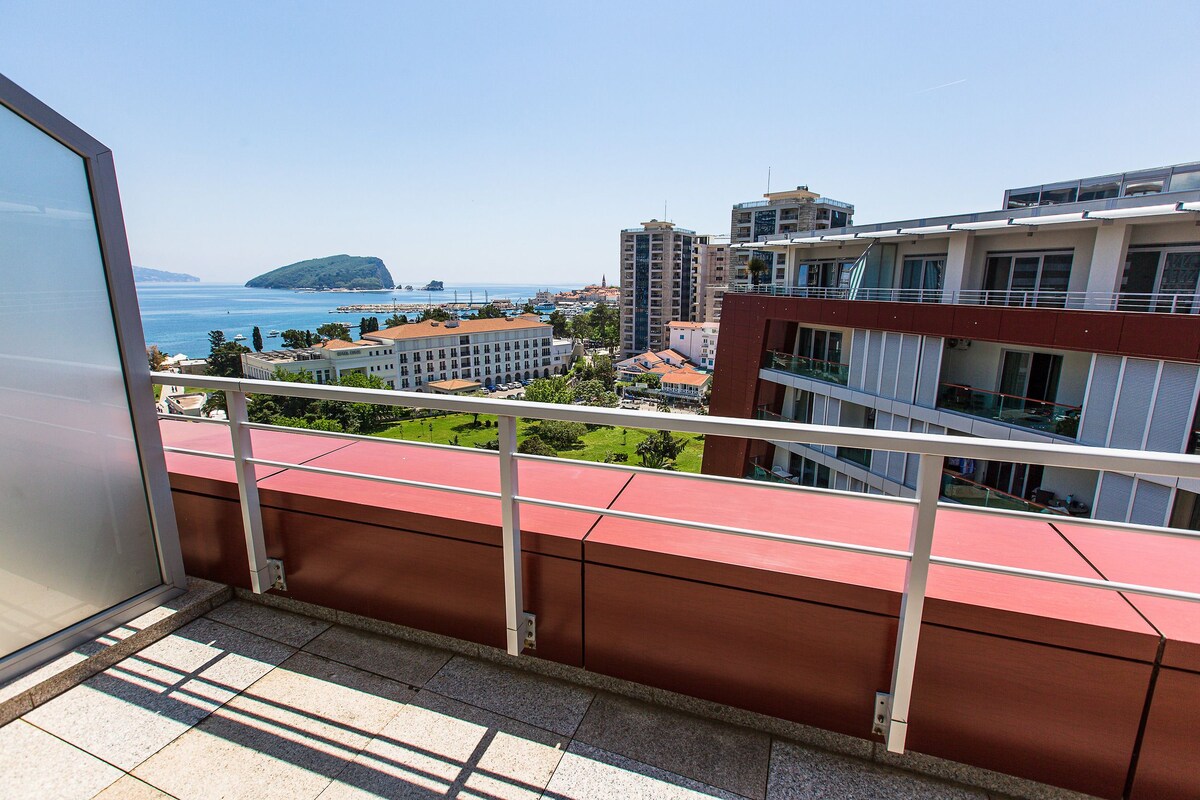 A balcony with a view of a coastal cityscape, including buildings and a distant island.