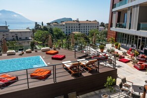 A rooftop pool area with lounge chairs and a view of the sea and mountains.