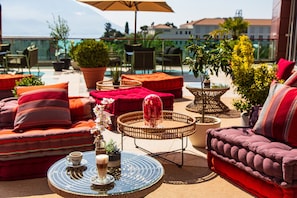 Terraza en la azotea con mobiliario exterior, plantas en macetas y vistas a edificios y un cuerpo de agua.