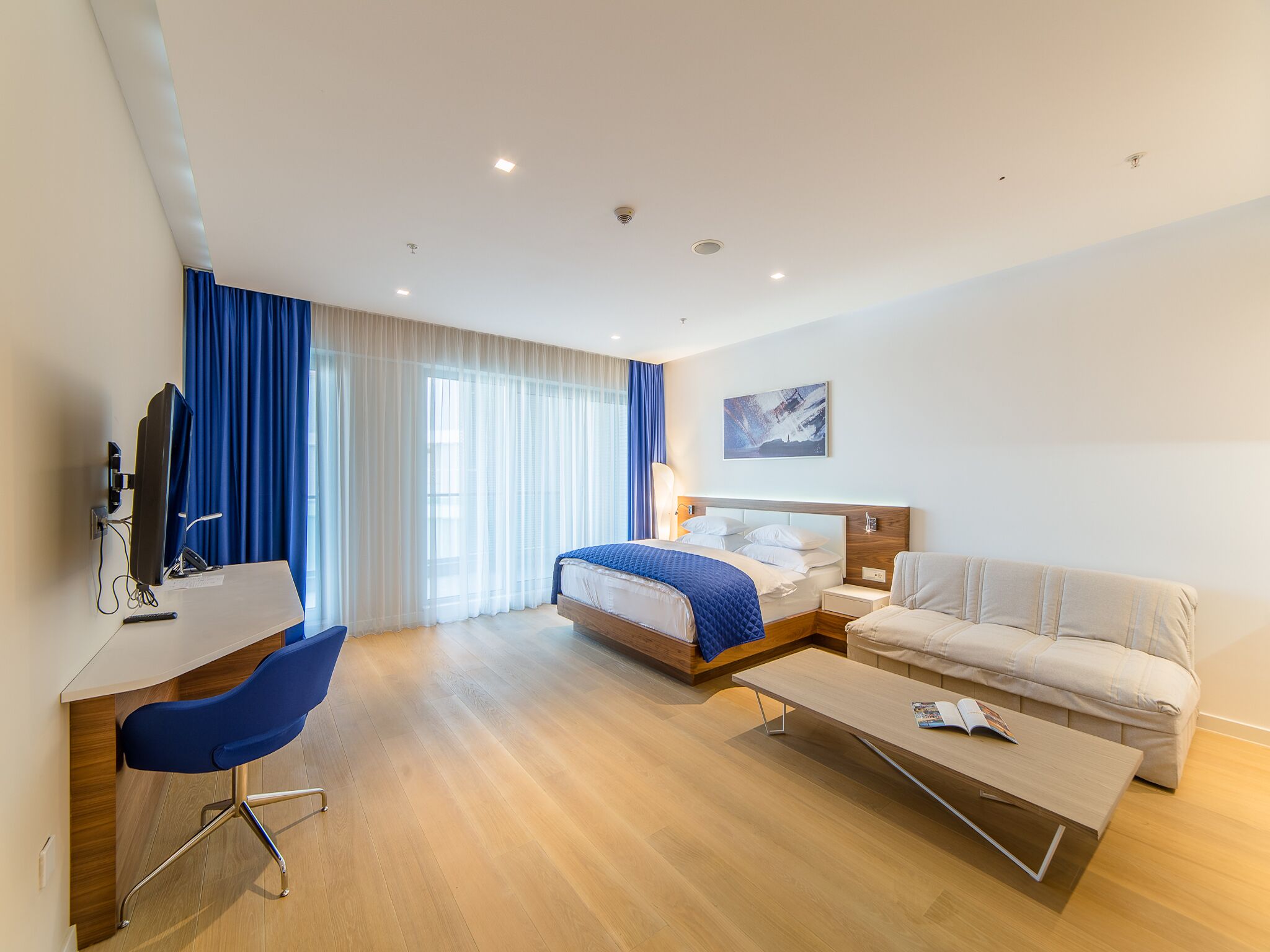 Ein modernes Hotelzimmer mit Bett, Schreibtisch, Stuhl, einer Couch und einem Gemälde an der Wand.