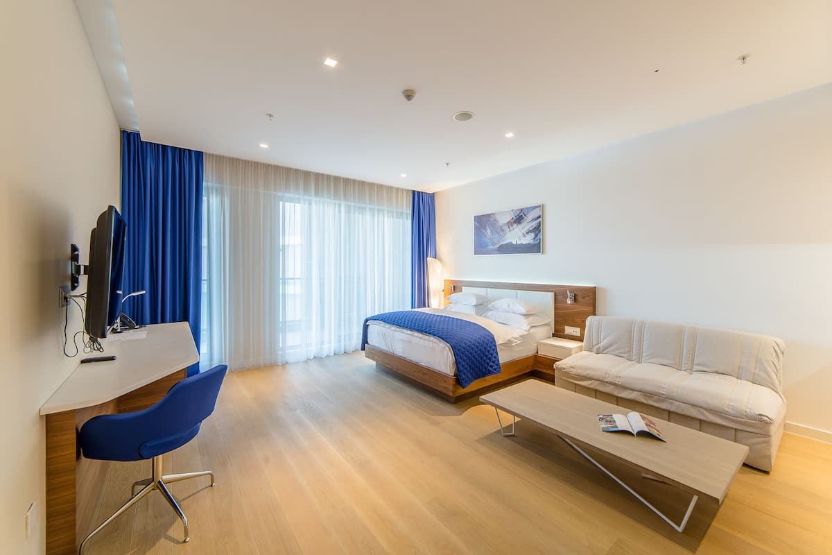 Une chambre d’hôtel moderne, équipée d’un lit, d’un bureau, d’une chaise, d’un canapé et d’un tableau au mur.