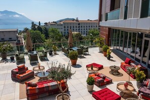 A rooftop terrace with outdoor seating, potted plants, and a view of the sea and buildings.