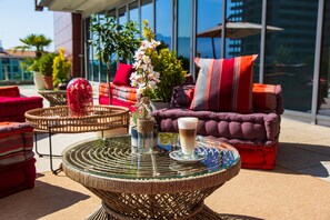 A wicker table with a glass top, a glass of beverage, and a vase with flowers. - Hotel Tq Plaza (Budva)